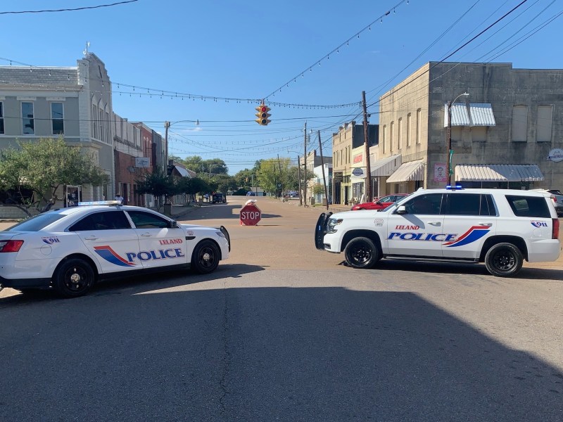 Two police cars parked next to each other in the middle of a four-way intersection.