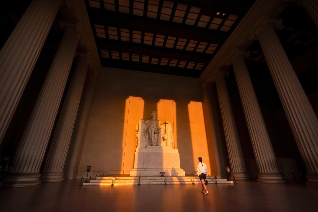A person looking at the Lincoln Memorial as the sunrise shines against it in columns