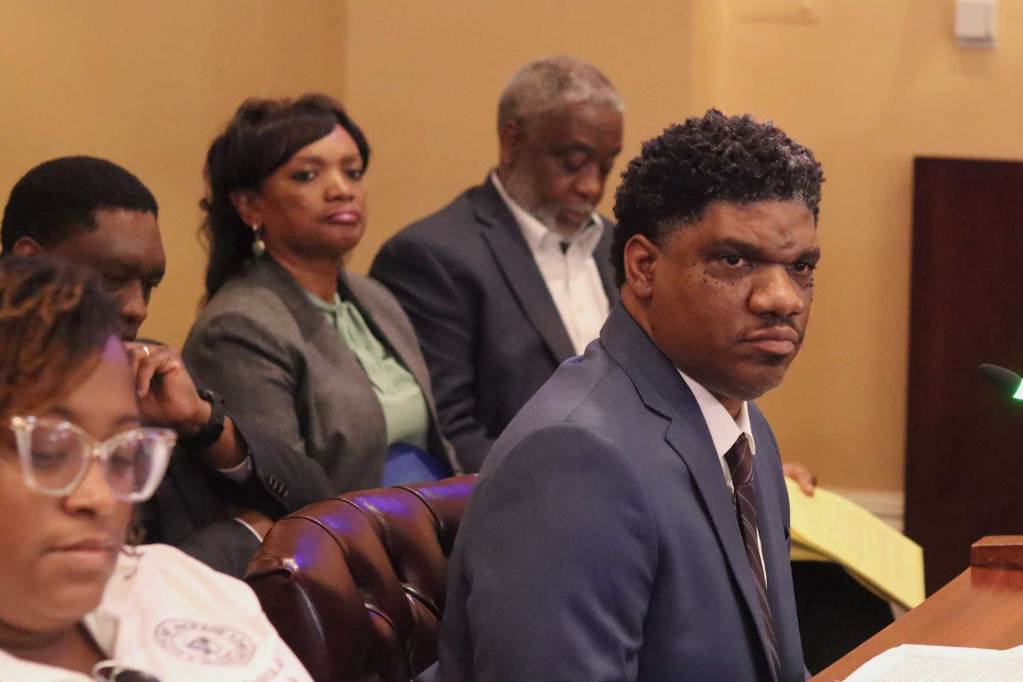 Lorenzo Anderson speaking at City Hall with others seated around him
