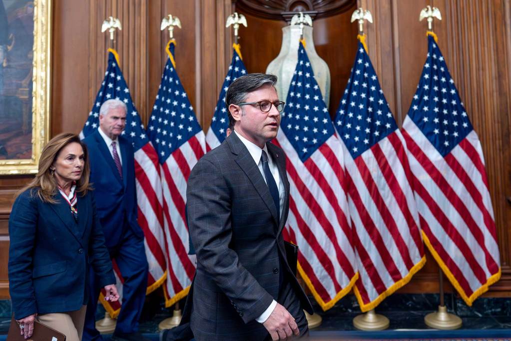 Mike Johnson walks past a row of standing US flags into a conference room