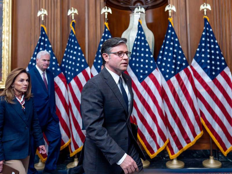 Mike Johnson walks past a row of standing US flags into a conference room