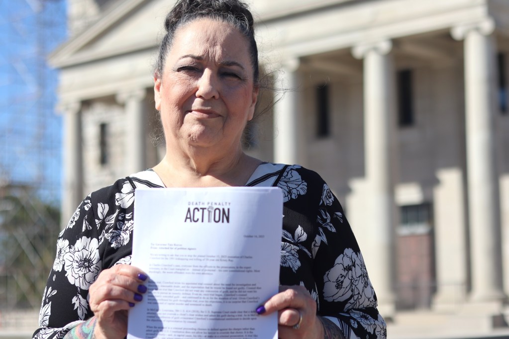 a woman holds up a letter with the words "Death Penalty Action" written in large letters at the top