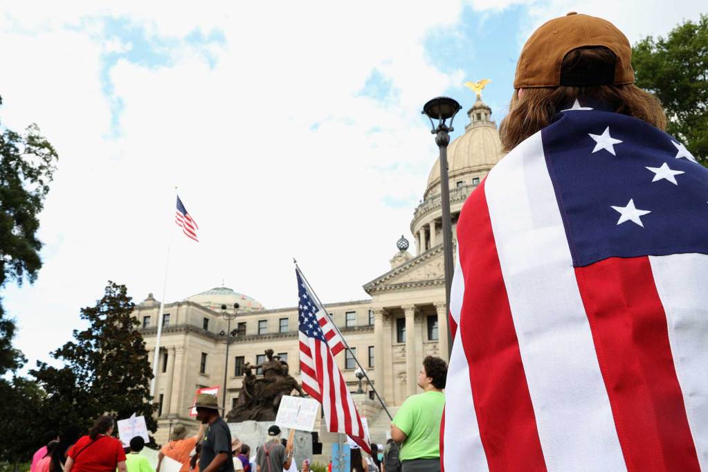 A protester wrapped in the US Flag stands at a rally