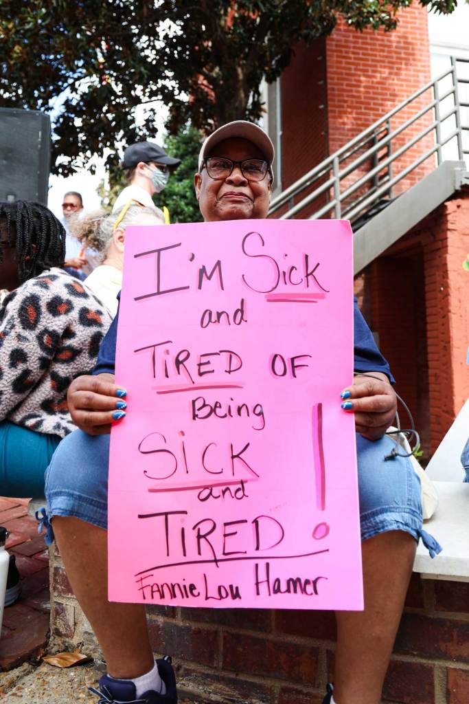 A woman holds up a pink sign that reads 'I'm Sick and Tired of Being Sick and Tired! - Fannie Lou Hamer'