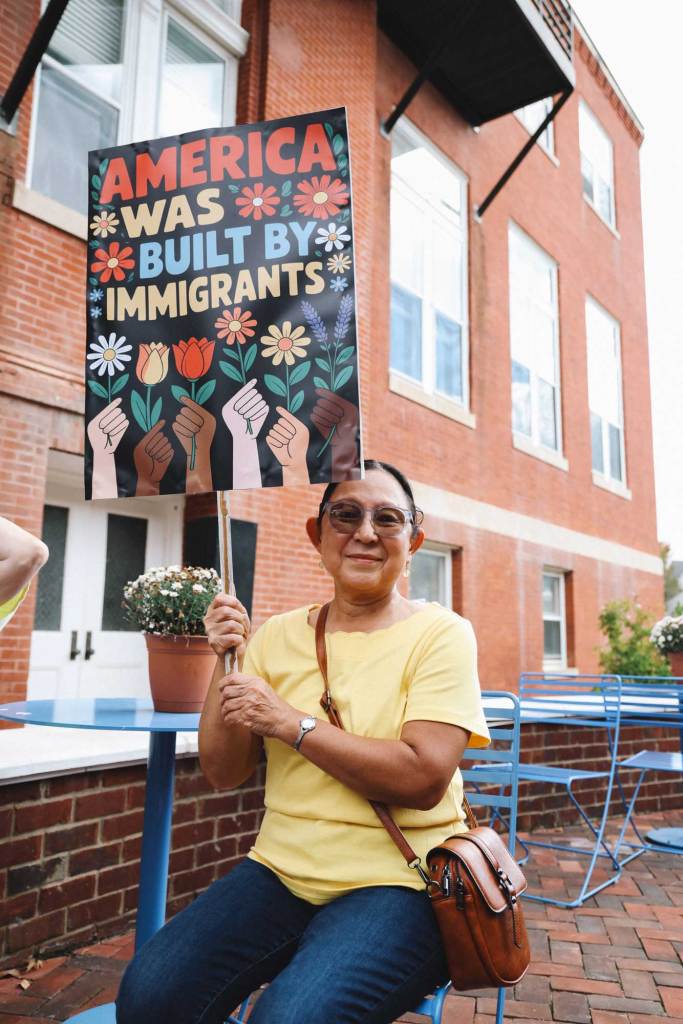 A woman holds a colorful sign of hands holding flowers that reads 'America was built by Immigrants'