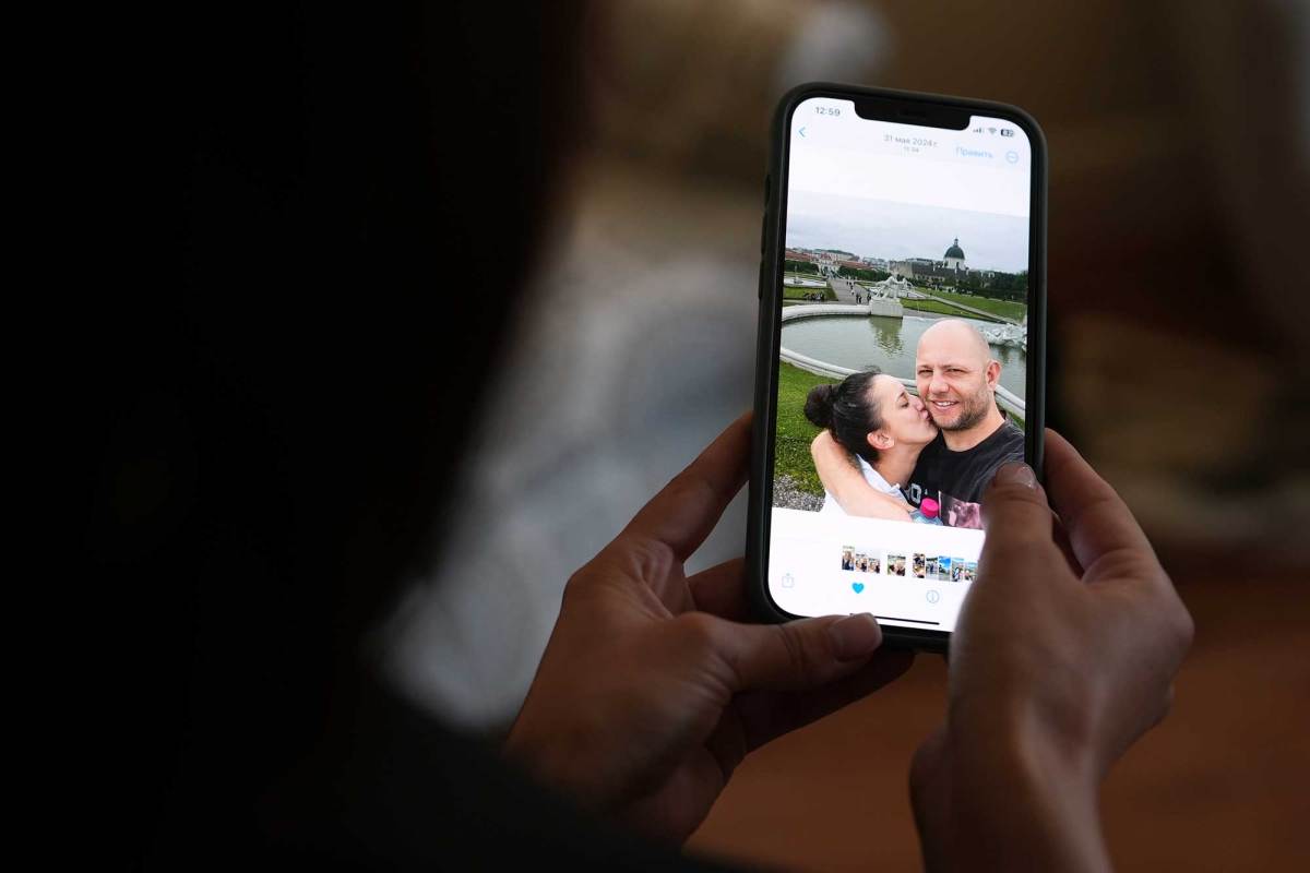 A pair of hands are seen holding a cell phone featuring a couple kissing outside