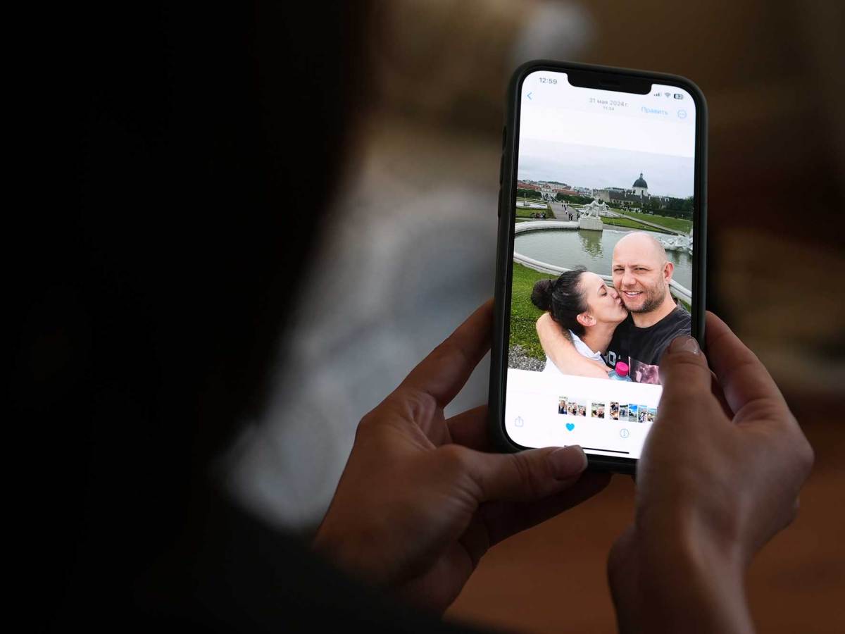 A pair of hands are seen holding a cell phone featuring a couple kissing outside
