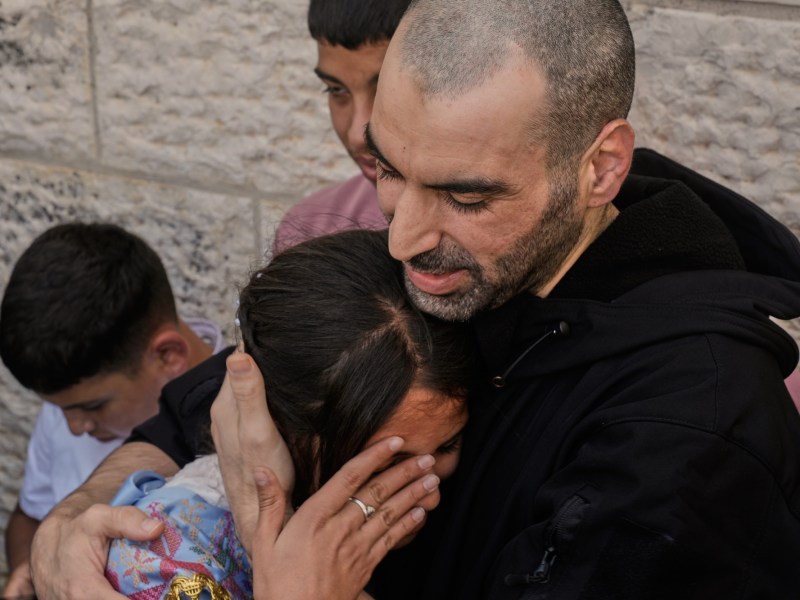 a woman leans on a man's chest, hugging him as she wipes tears from her eyes and he holds his hands around the back of her head and arms