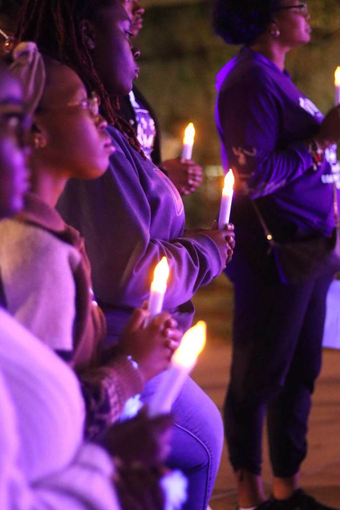 A group of people all hold electric candles at a nighttime vigil event