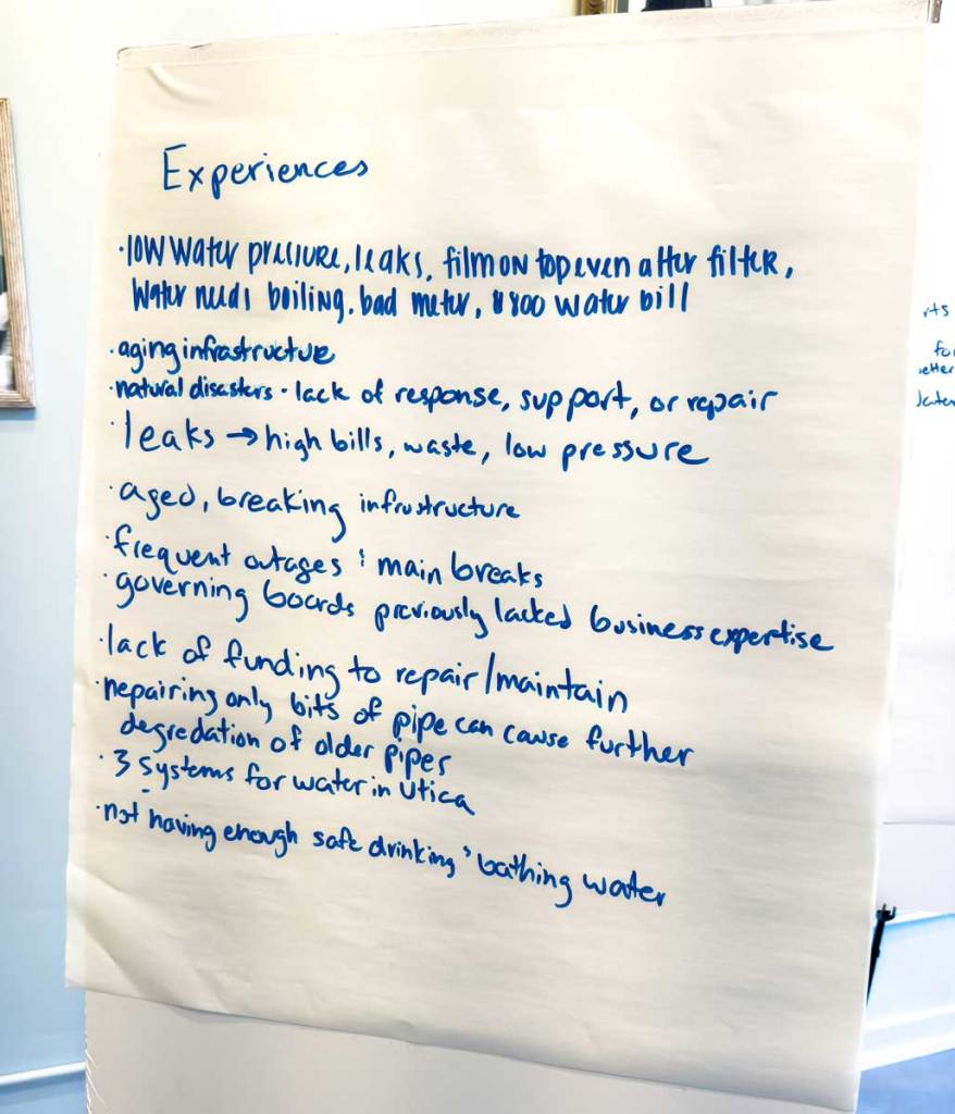 A large piece of paper on a stand lists residents experiences like aged, breaking infrastructure and frequent outages and main breaks