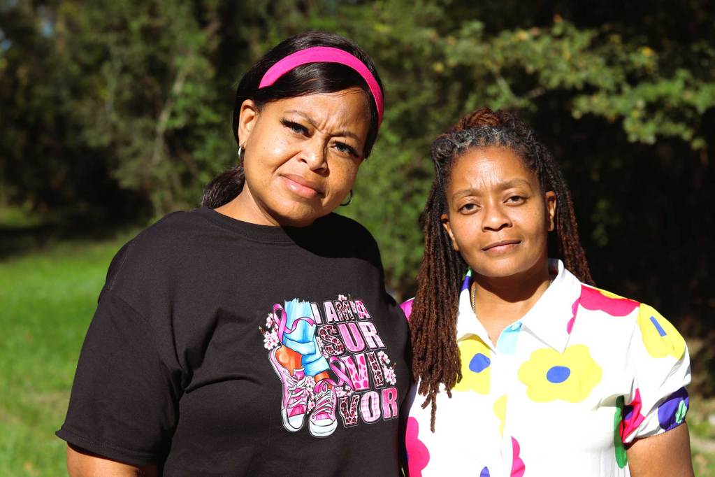 Two women stand outside together, one in black and pink and the other in a colorful floral print