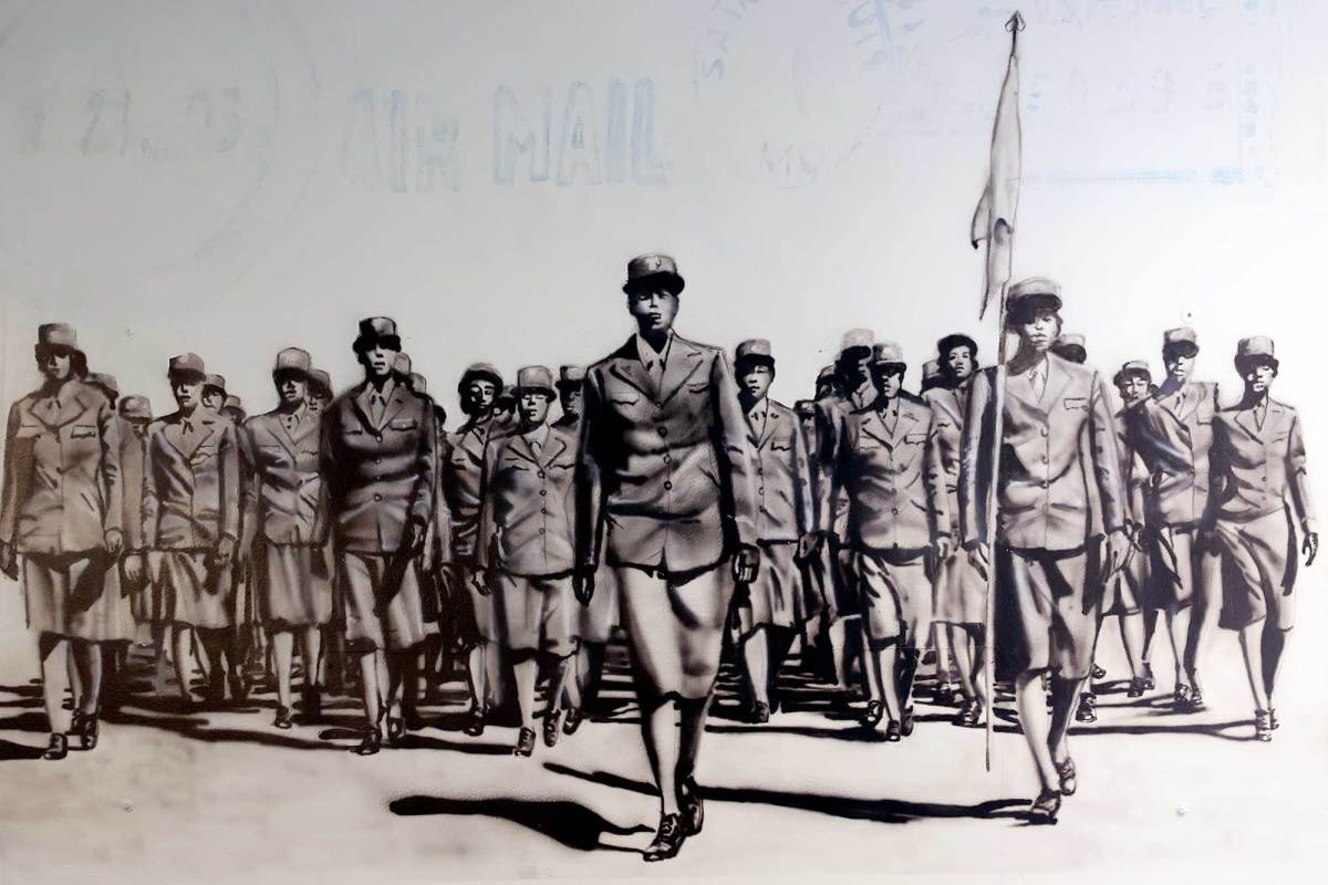 A black and white mural of a battalion of women in uniform, one is carrying a flag