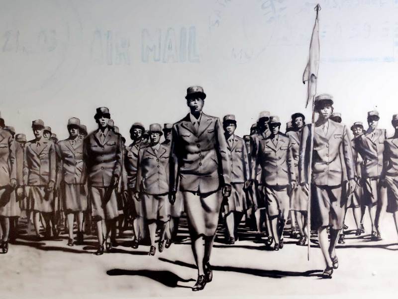 A black and white mural of a battalion of women in uniform, one is carrying a flag
