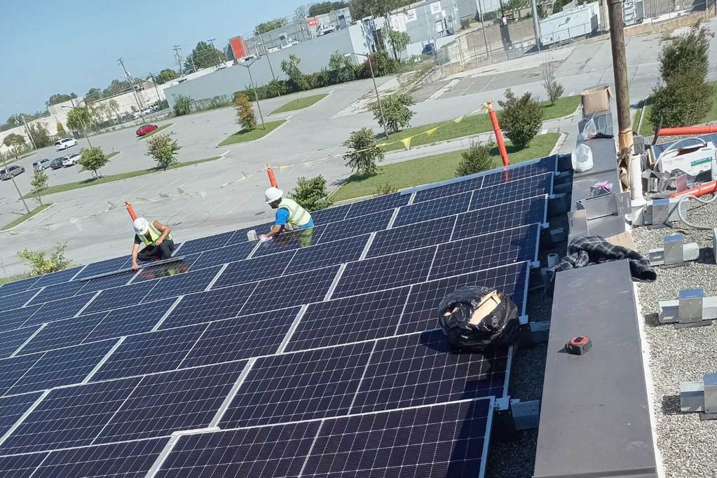 Two people in hardhats stand on a commercial roof and repair solar panels