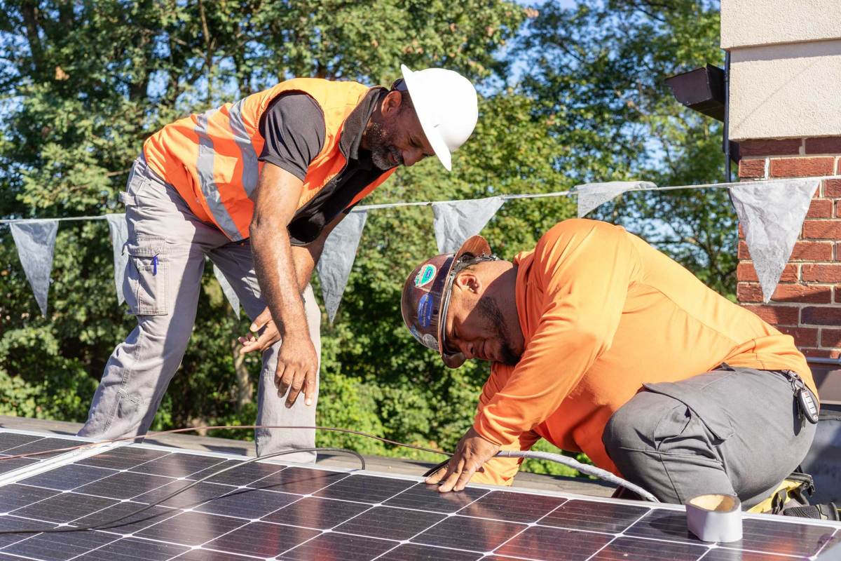 Two men in orange safety colors work on solar panels on a roof