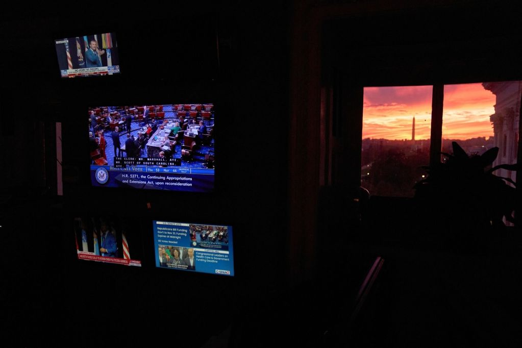 A view of the Washington Monument from a small window of a dark room, the room itself lit by tv monitors