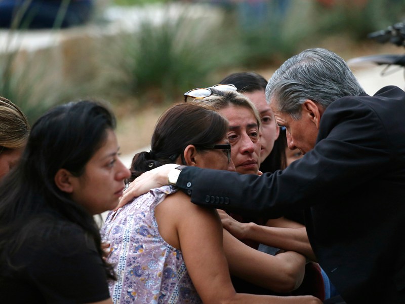 A grey-haired man comforts several women at an outside gathering