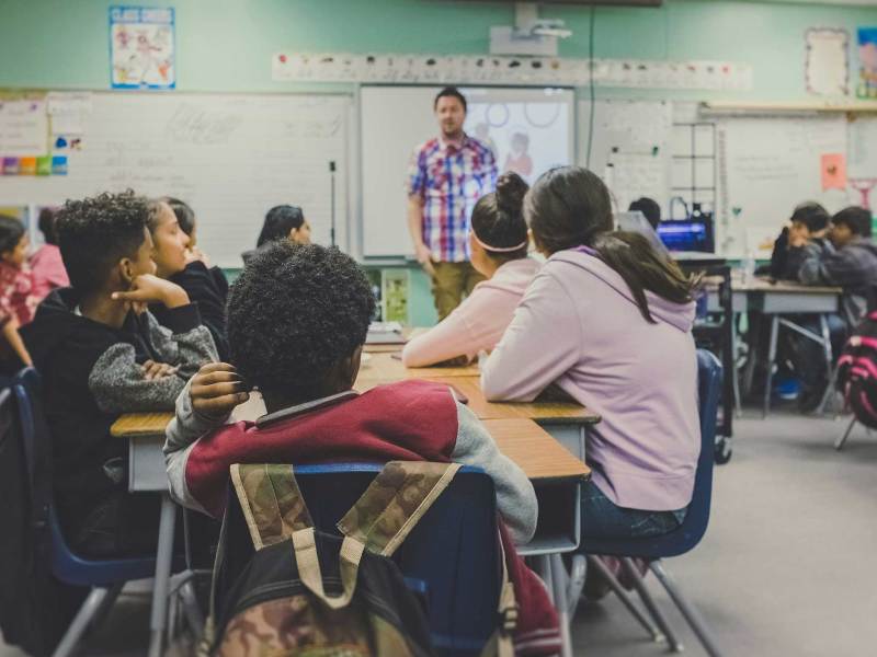 A classroom where students sit around tables in groups and look forward towards the teacher
