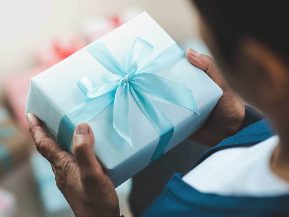 A person in a blue sweater holds a light blue wrapped gift box