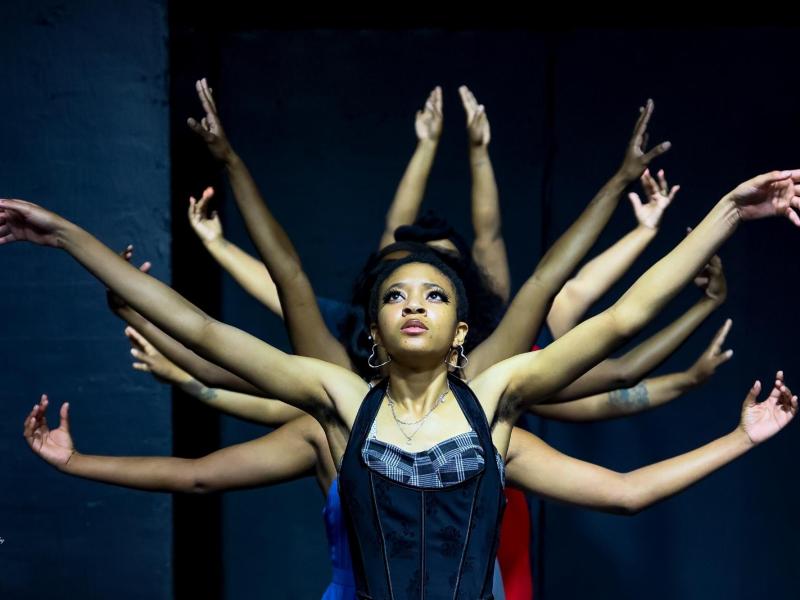 A dancer with her arms in the air, with several other dancers lined up behind her, each with their arms also extended in different positions.