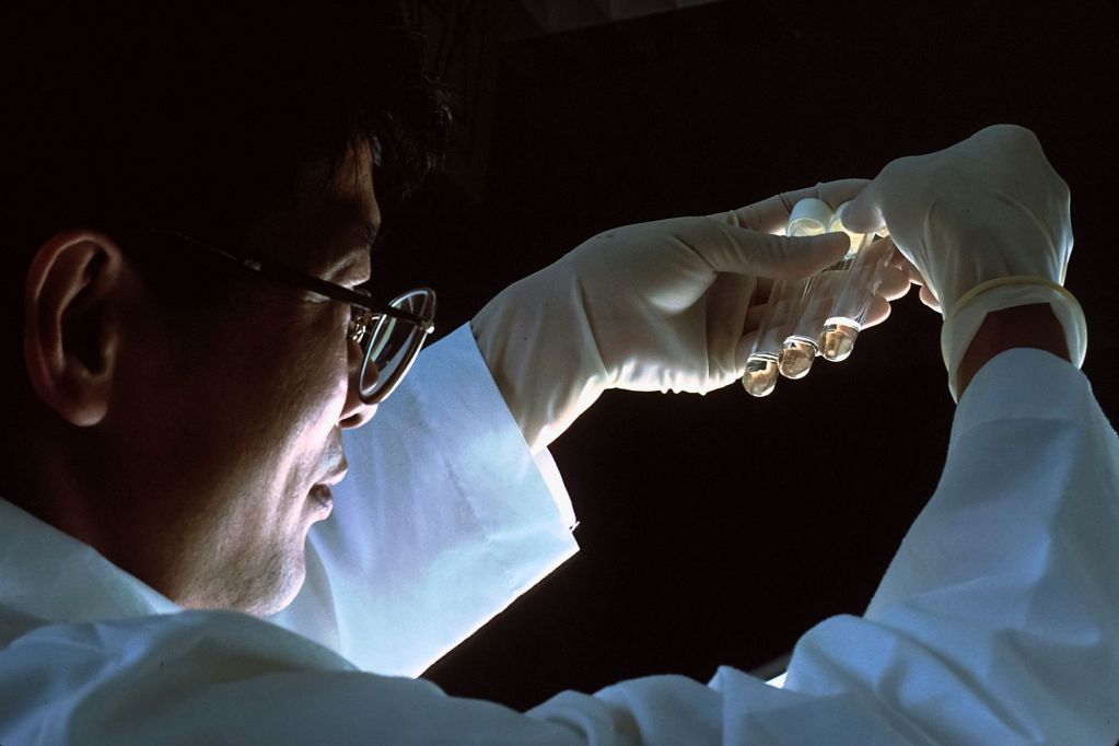 A man with glasses holding three glass test tubes in his hand.