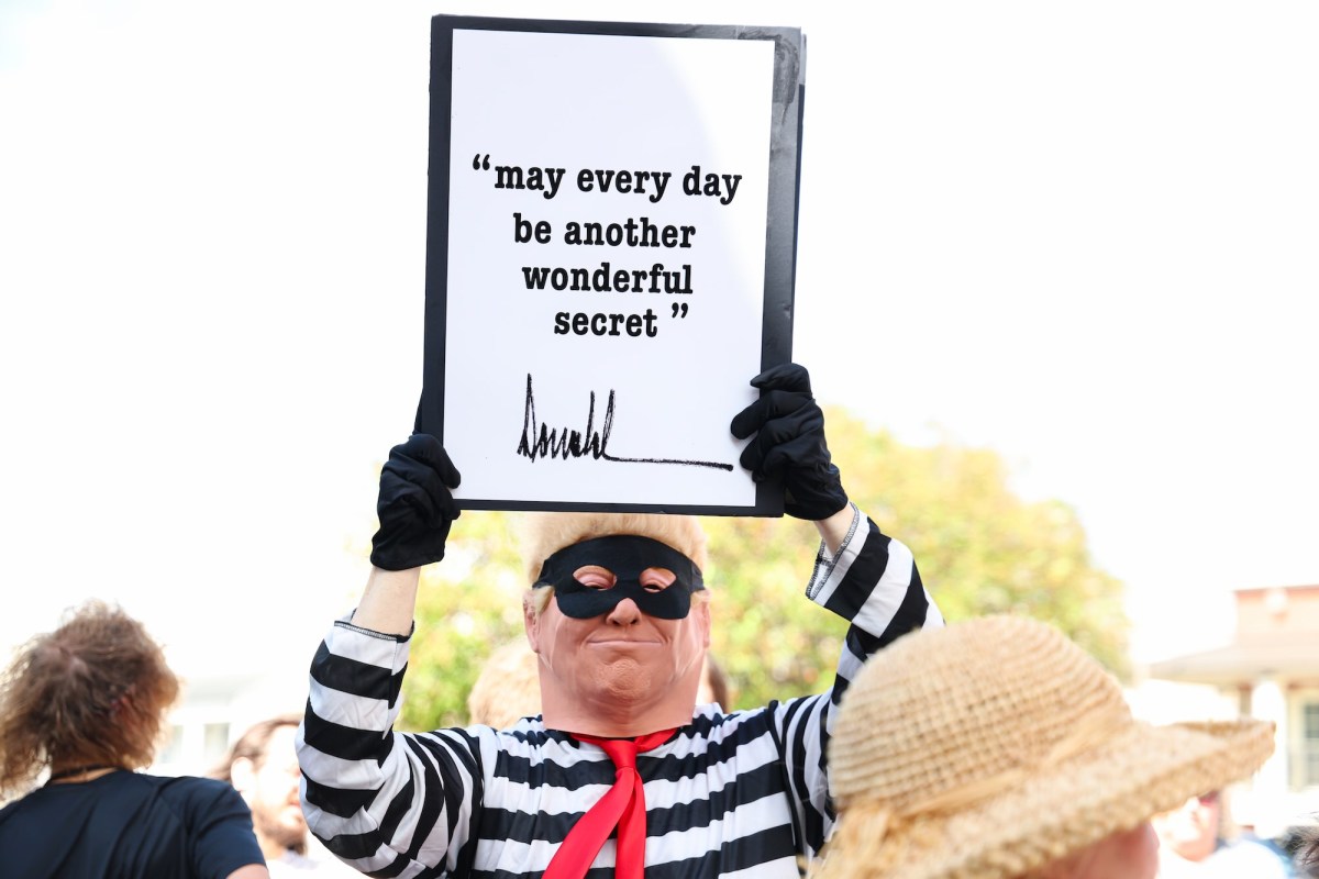 A protester dressed like Donald Trump in a cartoonish burglar costume holding up a sign that reads 'May every day be another wonderful secret' with Donald Trump's signature at the bottom