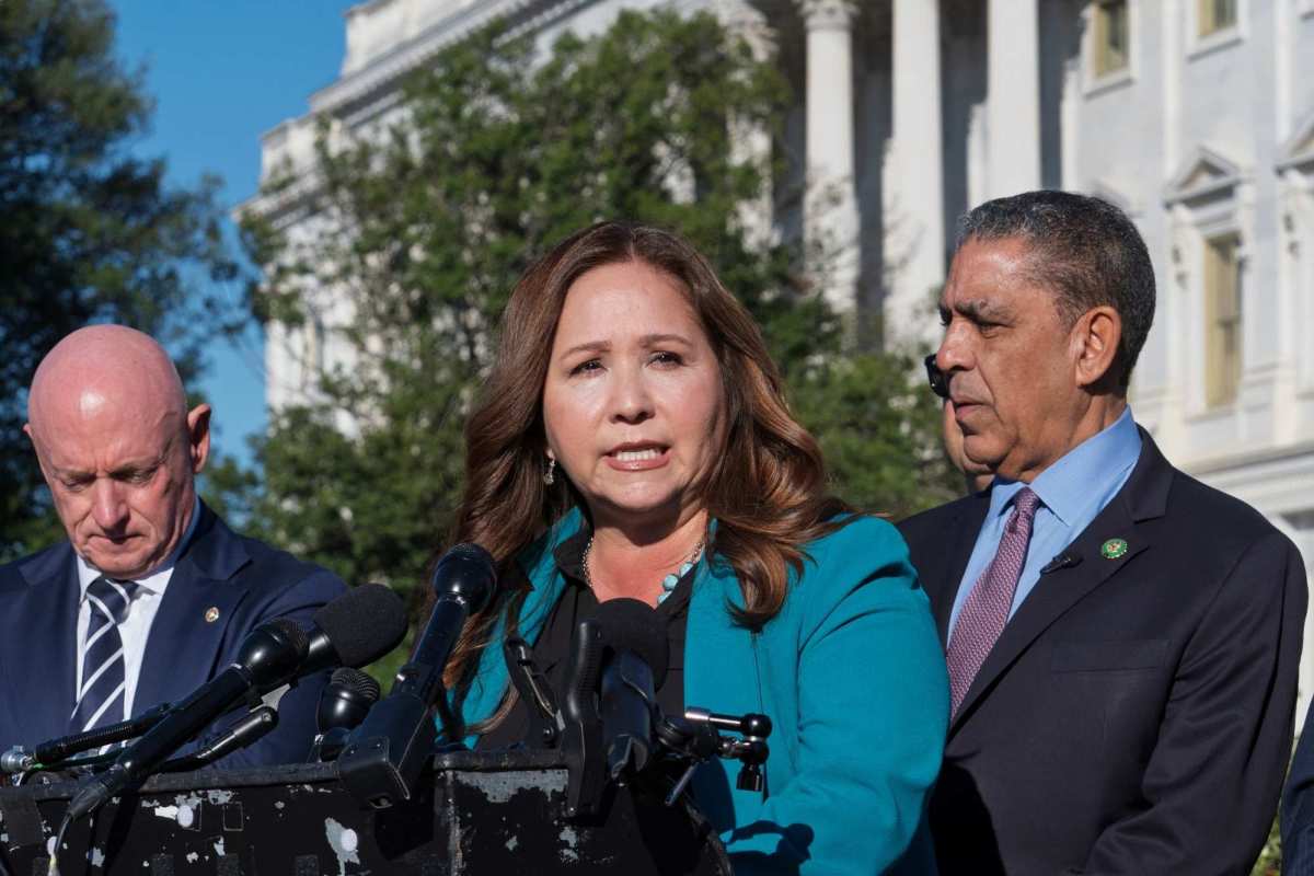 Adellita Grijalva speaking at a podium as two men on either side of her listen on.