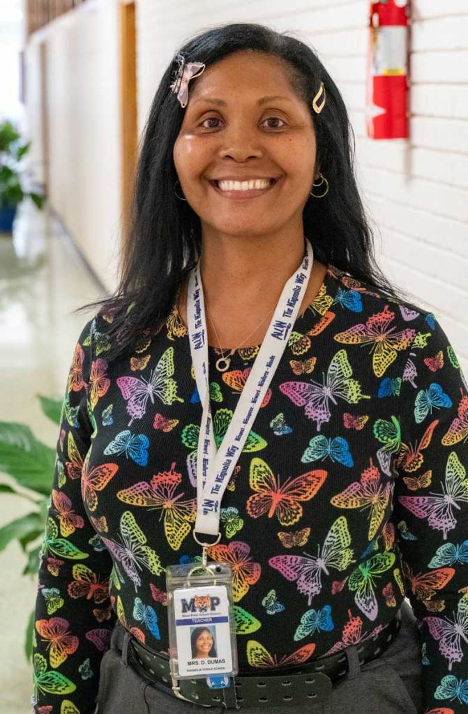 Woman smiling in a hallway, wearing a butterfly print shirt and school ID badge.