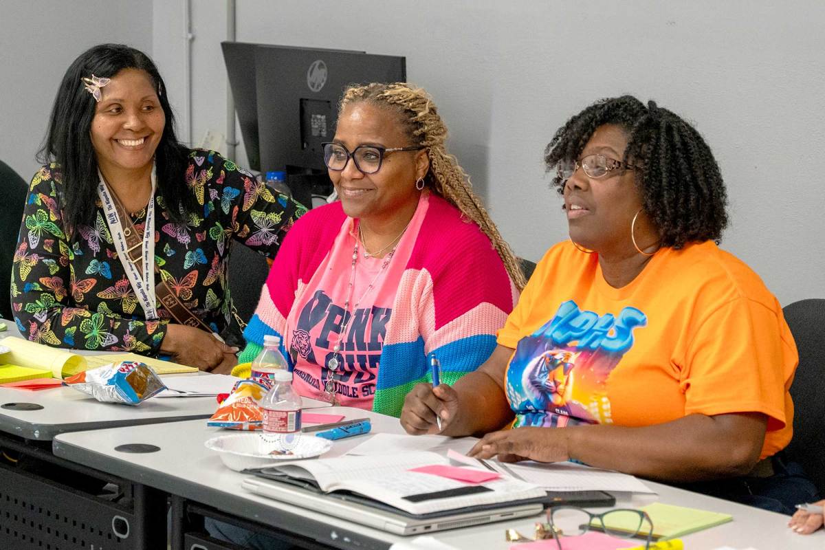 Three teachers seated at a table, discussing materials during a training session.