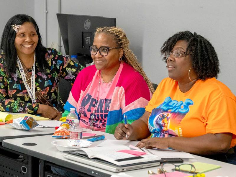 Three teachers seated at a table, discussing materials during a training session.