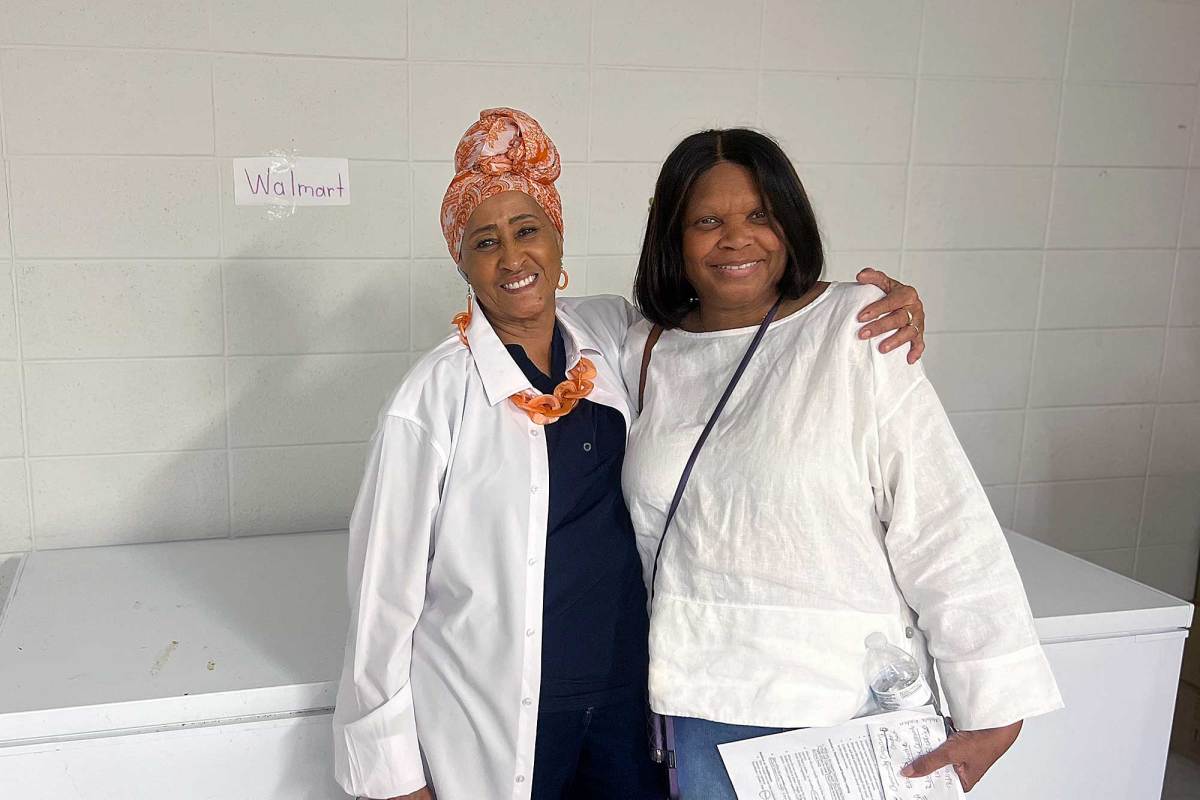 Two women pose in front of a large deep freezer