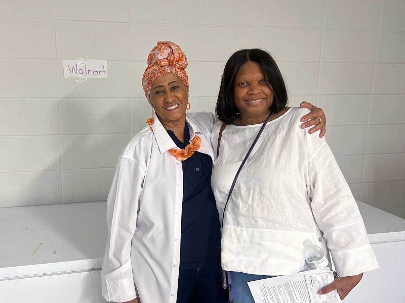 Two women pose in front of a large deep freezer