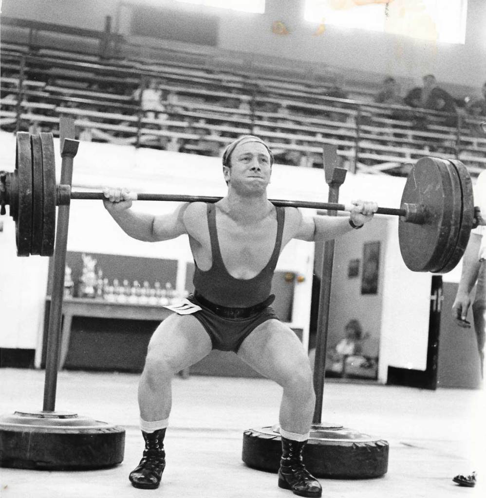 A man squatting with a barbell on his back, with weight plates on each side of the barbell.