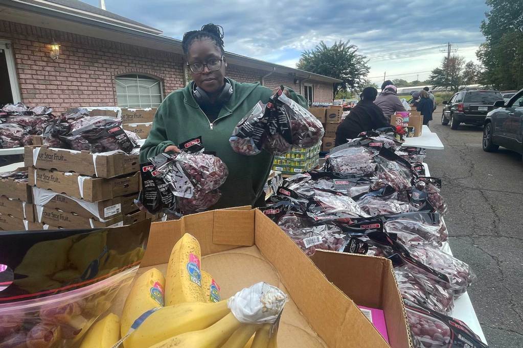 A woman in a green sweater sorts through bags of grapes at a food distribution event outside of a church