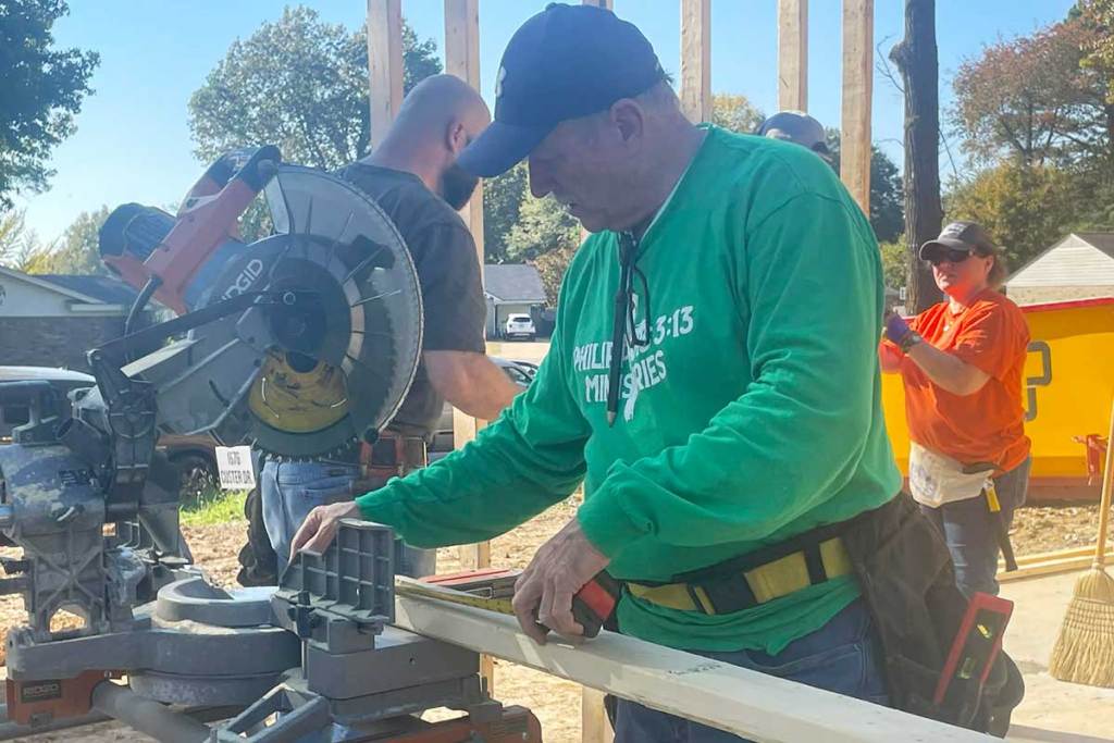 A man uses a saw to cut planks of wood as others work around him