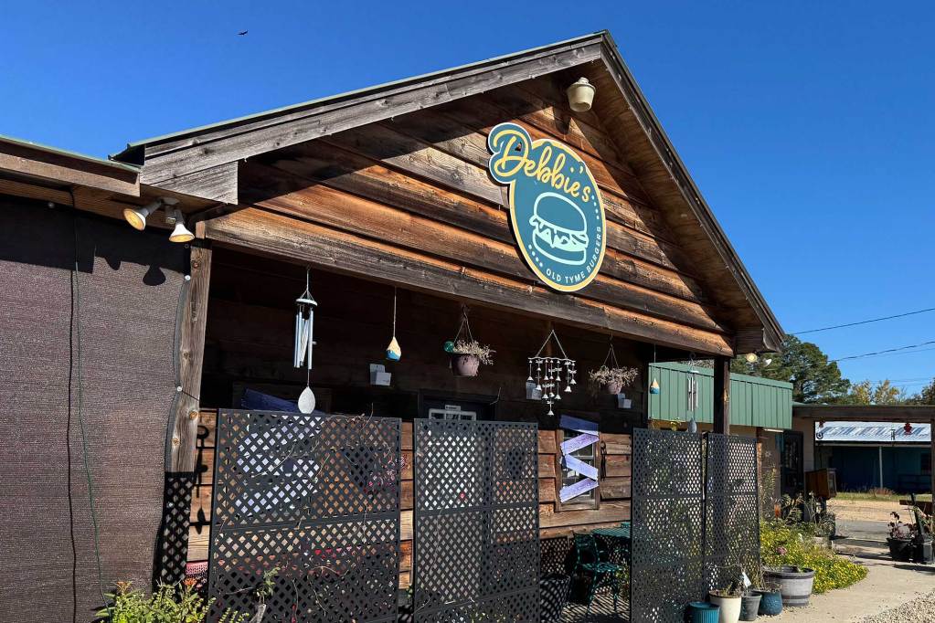 A wooden building is labeled with a round green sign that reads Debbie's and has simple lineart of a hamburger