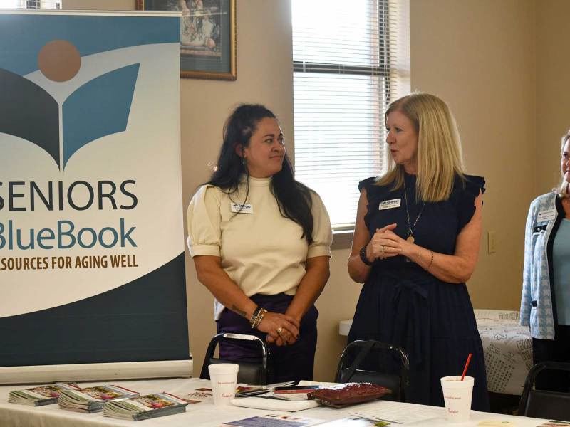Two women speaking next to a sign that reads “Seniors Blue Book, Resources for Aging Well.”