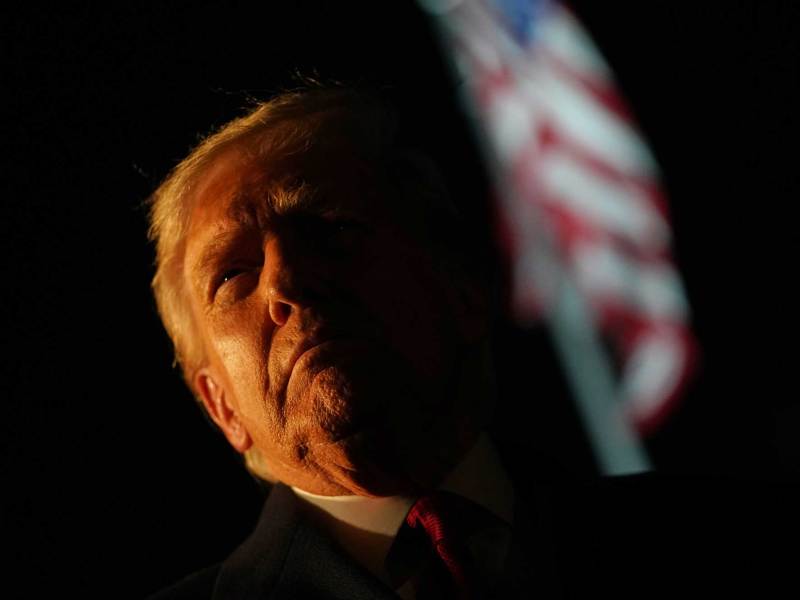 Donald Trump outside at night, dramatically lit on one side of his face only