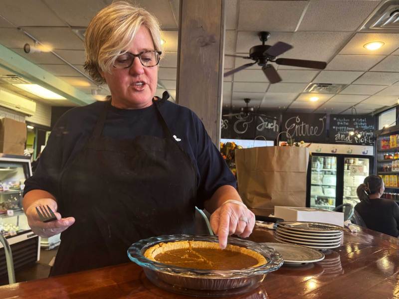A woman wearing an apron checking out a pie at a counter inside a restaurant.