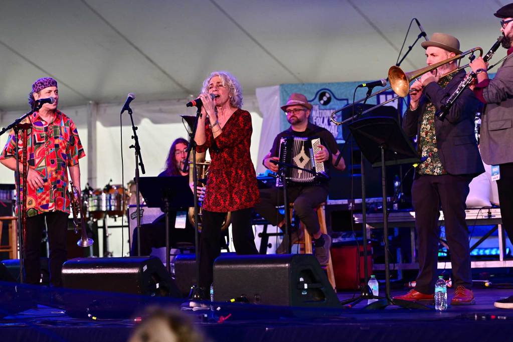 A woman sings in the microphone on stage as a band plays all around her with various instruments