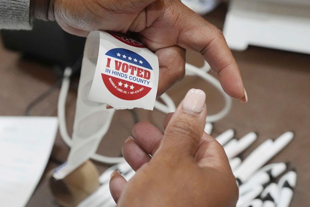 A pair of hands holds a reel of I Voted stickers and preps them for voters