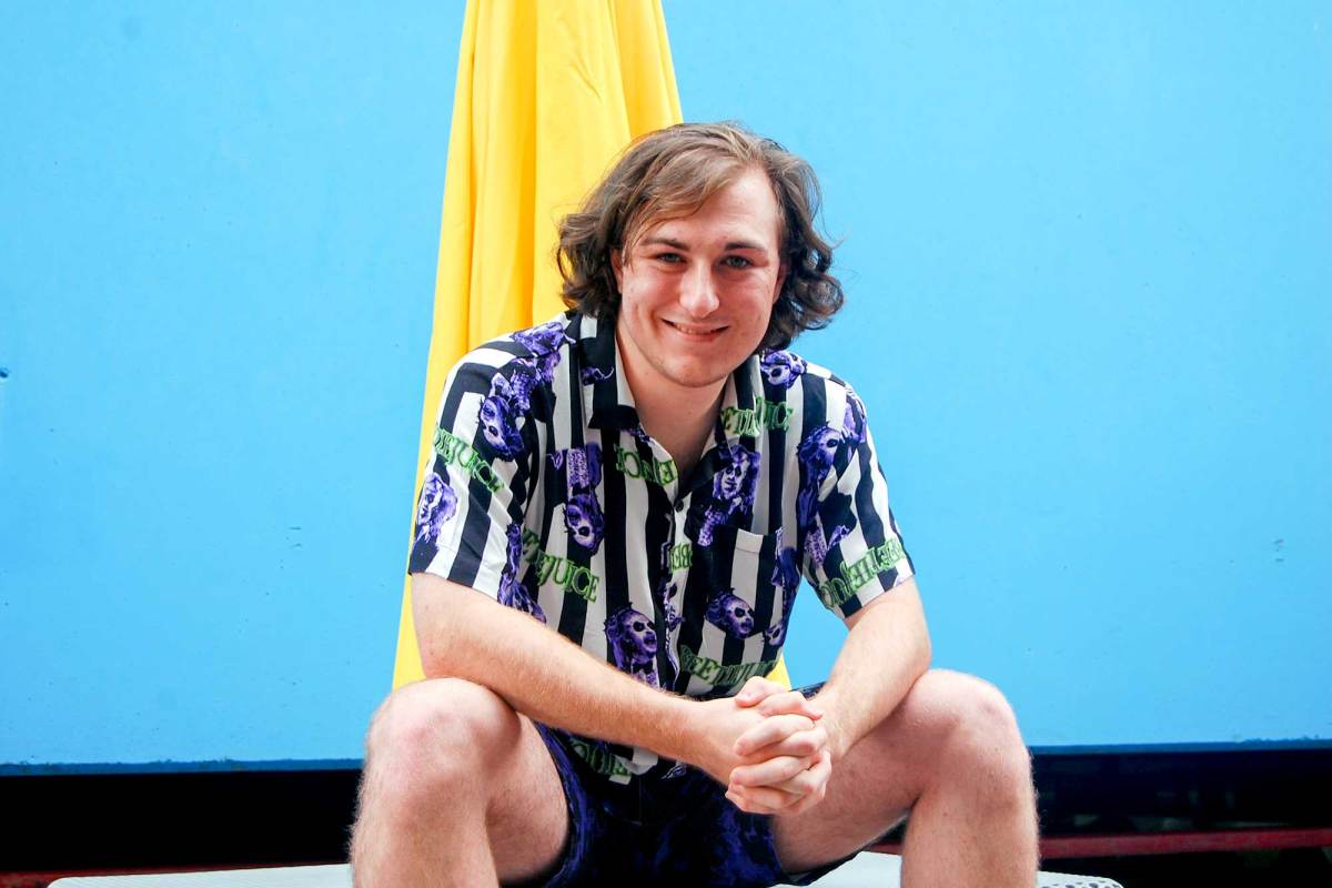 A man in a colorful striped shirt sits in front of a blue wall