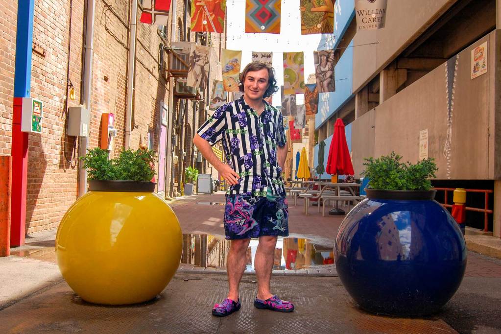 A man in a colorful striped shirt stands in an alleyway between two large round planters
