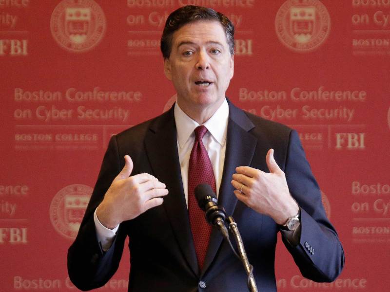 Former FBI Director James Comey speaking in front of a red wall that reads Boston Conference on Cyber Security