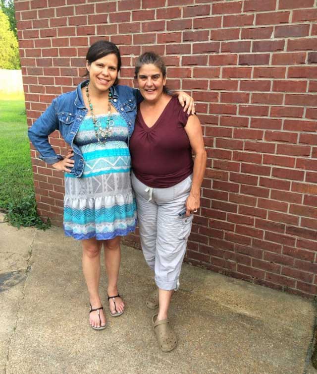 A mother and daughter pose together in front of a red brick wall outside
