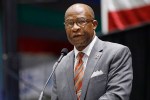 A Black man in a gray suit with glasses standing at a podium