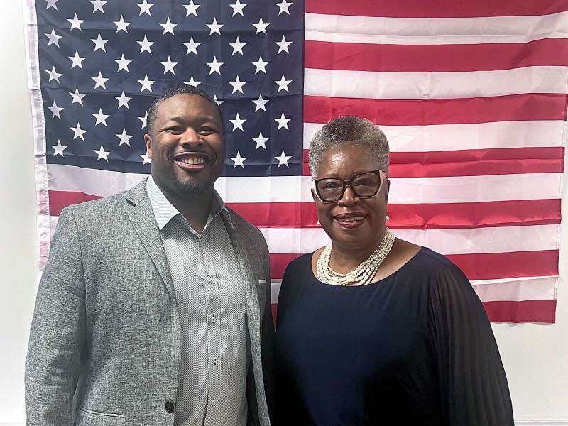 A man and a woman stand together in front of a US Flag