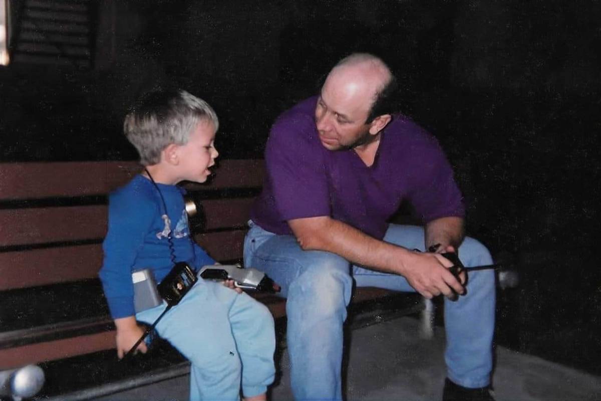 A father and son sit on a bench outside at night, walkie talkies in hand