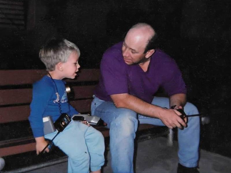 A father and son sit on a bench outside at night, walkie talkies in hand