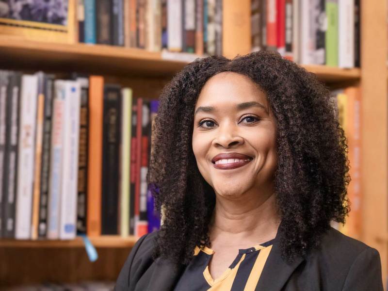 LaWanda Dickens smiles in front of a large bookcase filled with books
